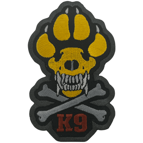 A velcro patch with crossbones and the paw of a working dog that is yellow. The crossbones are gray. The word "K9" is embroidered in red.